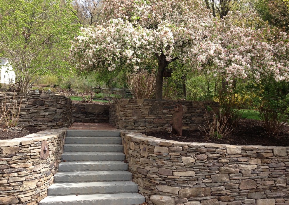 This is an example of a large classic back driveway partial sun garden for spring in New York with a retaining wall and brick paving.