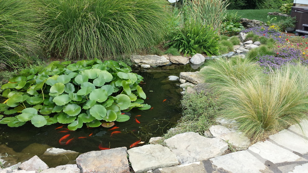 Réalisation d'un grand jardin arrière tradition avec un bassin, une exposition ensoleillée et des pavés en pierre naturelle.