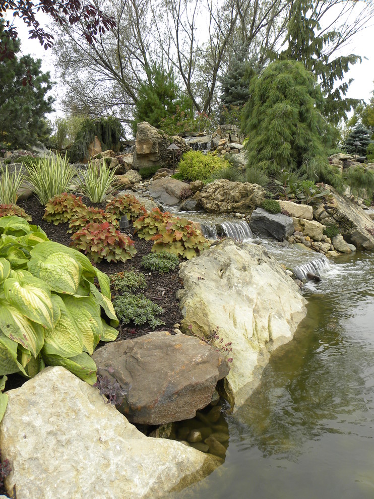 Exemple d'un très grand jardin arrière chic l'été avec un point d'eau, une exposition partiellement ombragée et des pavés en pierre naturelle.