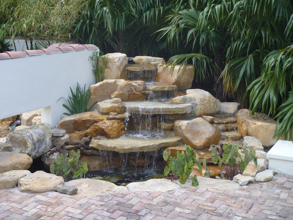 Aménagement d'un jardin arrière exotique avec un bassin et des pavés en pierre naturelle.