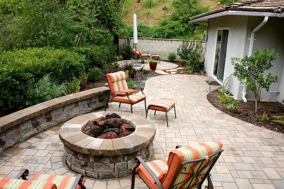 Cette image montre une petite terrasse arrière minimaliste avec un foyer extérieur et des pavés en béton.