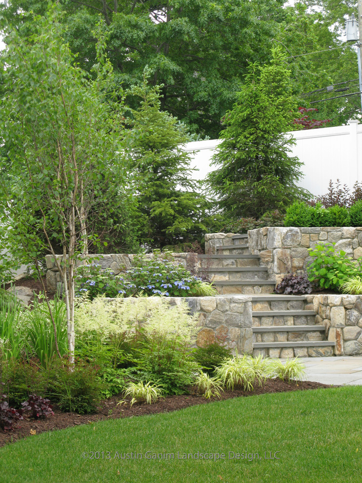 Aménagement d'un jardin arrière contemporain l'été avec un mur de soutènement, une exposition partiellement ombragée et des pavés en pierre naturelle.