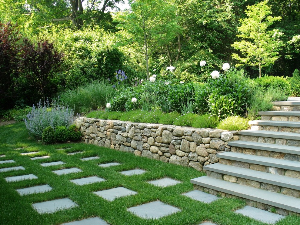 Réalisation d'un grand jardin arrière tradition avec une exposition partiellement ombragée, des pavés en pierre naturelle et un mur de soutènement.