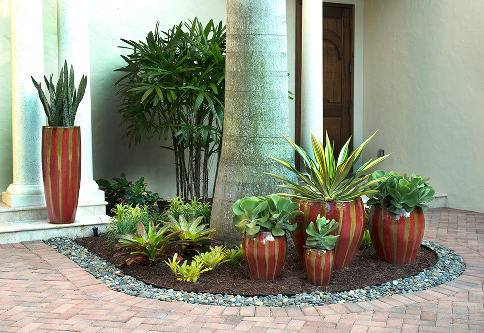 Inspiration för en stor tropisk trädgård i delvis sol framför huset, med utekrukor och marksten i tegel