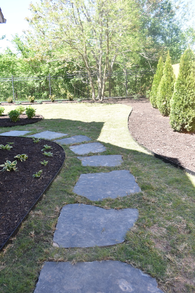 This is an example of a large traditional partial sun backyard stone landscaping in Other.