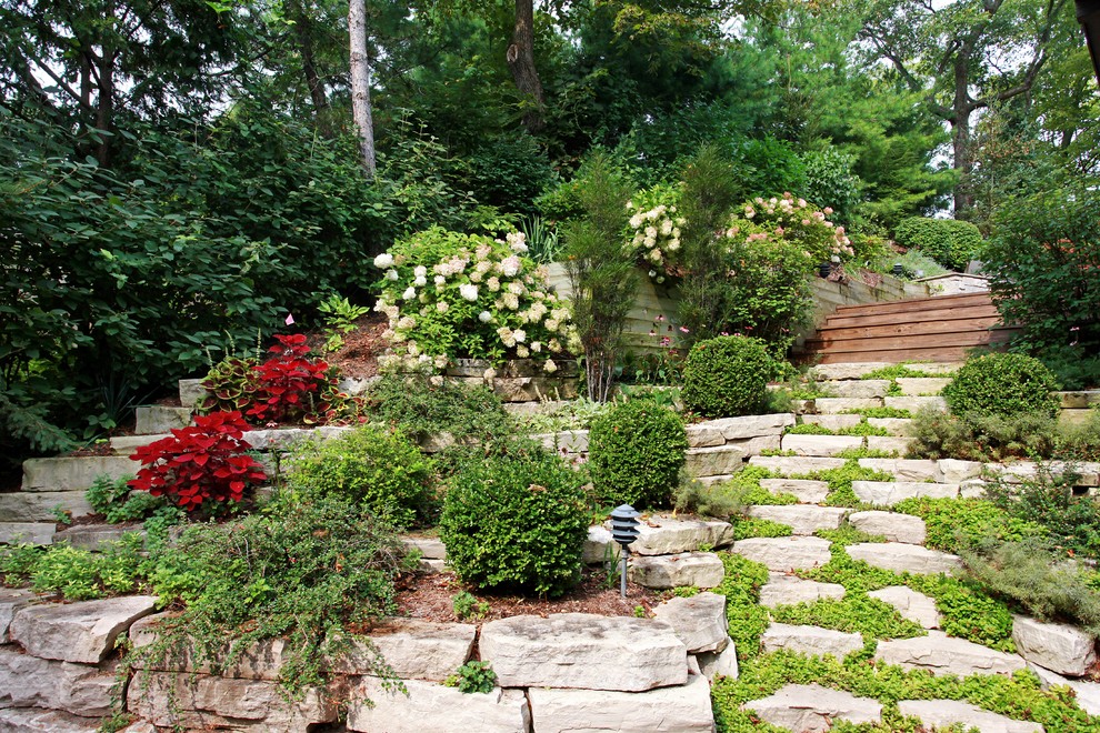 Cette image montre un grand jardin arrière design avec une exposition partiellement ombragée et des pavés en pierre naturelle.