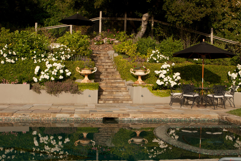 Exempel på en stor klassisk trädgård i full sol i slänt, med utekrukor och naturstensplattor