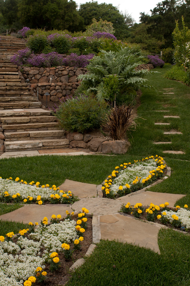 На фото: большой солнечный регулярный сад на склоне в классическом стиле с подпорной стенкой, хорошей освещенностью и покрытием из каменной брусчатки