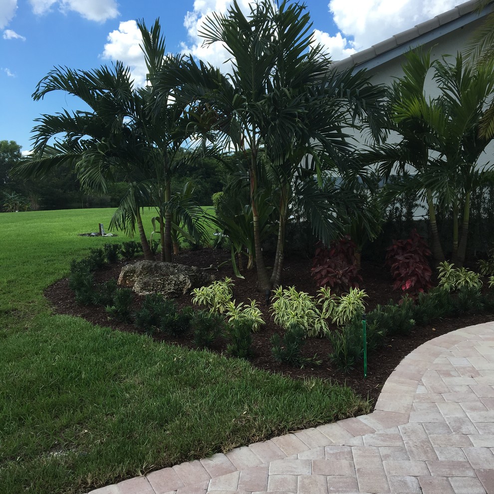 Large contemporary front xeriscape full sun garden in Miami with natural stone paving.