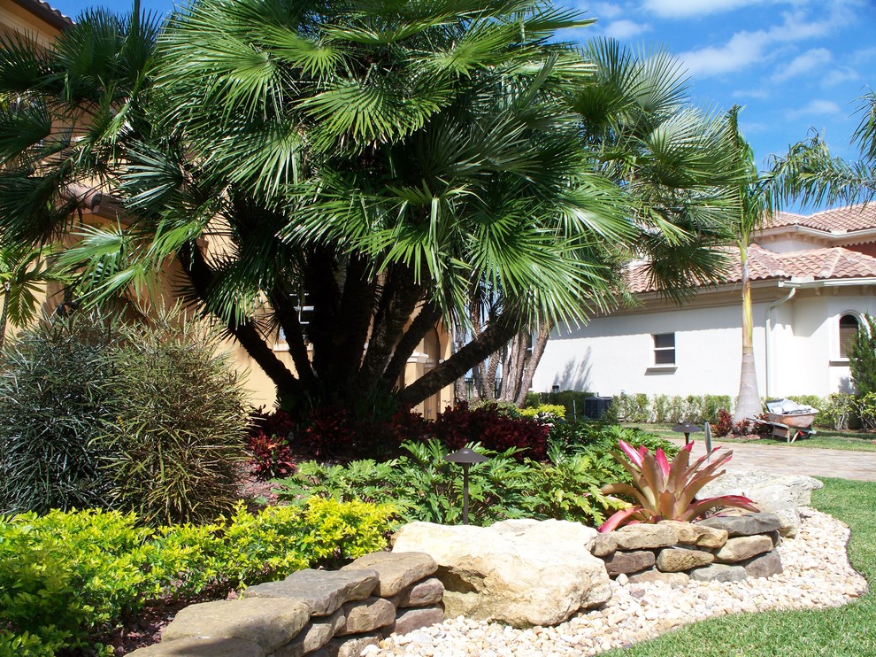 This is an example of a large world-inspired front driveway full sun garden in Miami with natural stone paving.