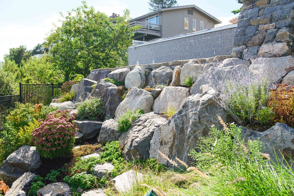 Cette image montre un jardin arrière marin de taille moyenne avec un mur de soutènement et des pavés en pierre naturelle.