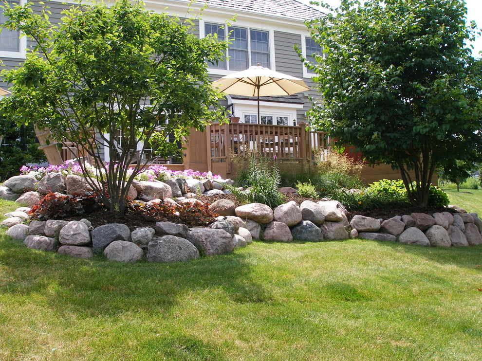Foto di un piccolo giardino tradizionale esposto in pieno sole dietro casa in estate con un muro di contenimento e pavimentazioni in pietra naturale