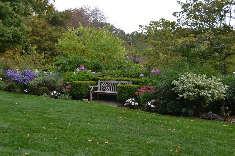 Exempel på en mellanstor klassisk formell trädgård i delvis sol längs med huset på sommaren, med naturstensplattor
