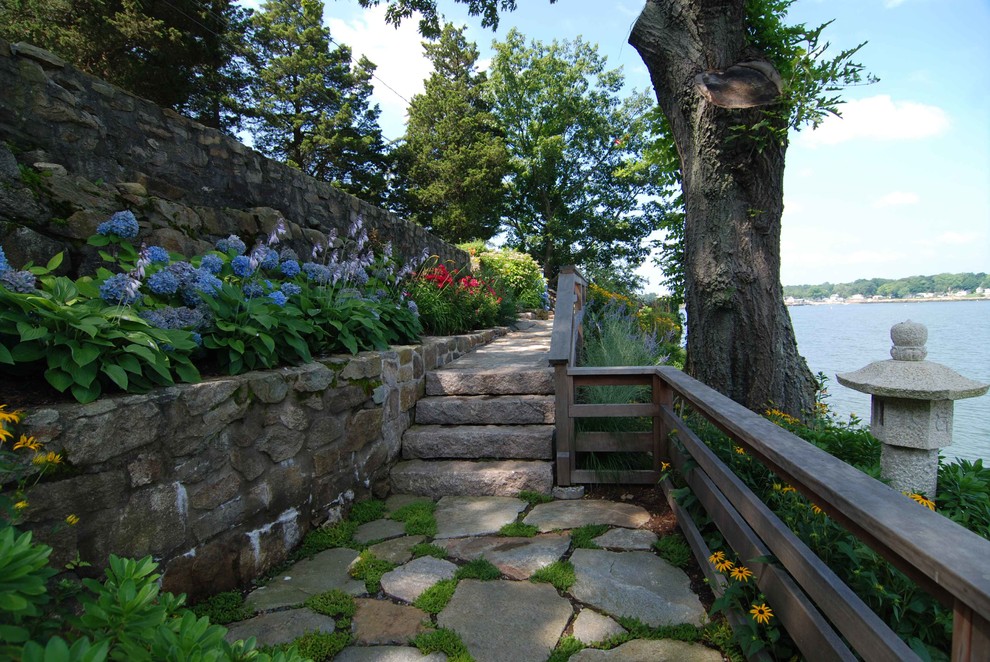 Cette photo montre un jardin bord de mer de taille moyenne et l'été avec un mur de soutènement, une exposition ombragée, une pente, une colline ou un talus et des pavés en pierre naturelle.