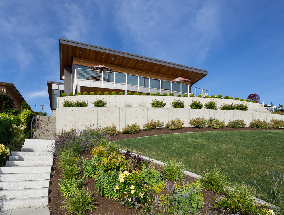 Diseño de jardín minimalista grande en patio delantero con muro de contención, exposición total al sol y adoquines de hormigón