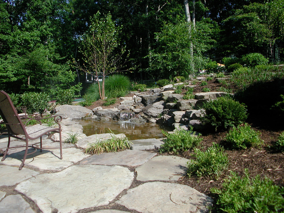 Réalisation d'un petit jardin arrière tradition l'été avec un bassin, une exposition ensoleillée et des pavés en pierre naturelle.