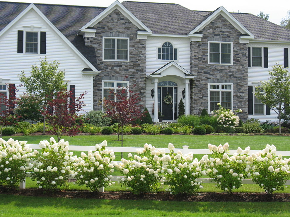Photo of a large traditional front formal full sun garden in Burlington with a potted garden and mulch.