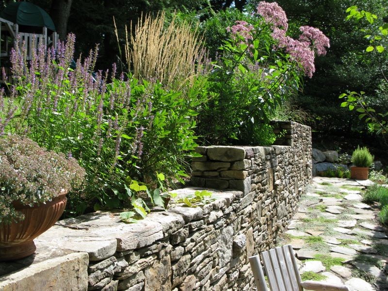 Imagen de jardín actual de tamaño medio en verano en ladera con muro de contención, exposición total al sol y adoquines de piedra natural