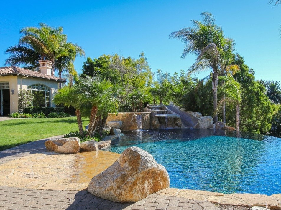 Imagen de jardín tropical grande en patio trasero con adoquines de piedra natural, jardín francés y exposición total al sol