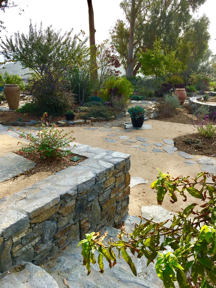 Idee per un grande giardino xeriscape mediterraneo esposto in pieno sole dietro casa con un muro di contenimento e pavimentazioni in pietra naturale
