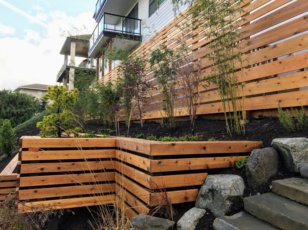 Photo of a large modern sloped partial sun garden in Portland with a retaining wall.