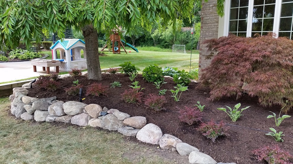 This is an example of a mid-sized traditional partial sun front yard mulch retaining wall landscape in Detroit for summer.