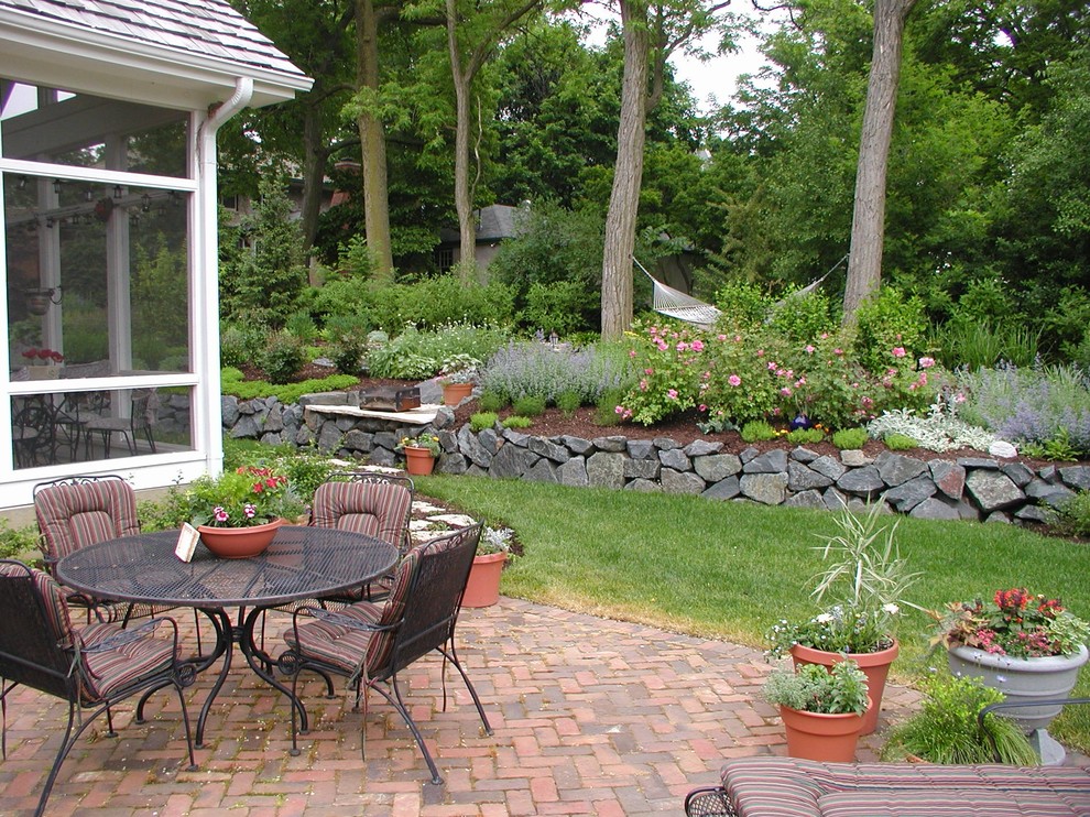 Foto di un giardino formale tradizionale esposto in pieno sole dietro casa in estate con un muro di contenimento e pavimentazioni in mattoni