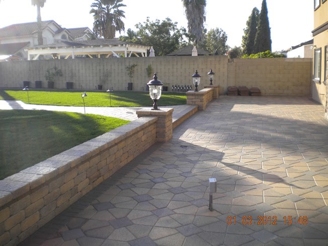 Modelo de jardín mediterráneo de tamaño medio en patio trasero con muro de contención y adoquines de hormigón
