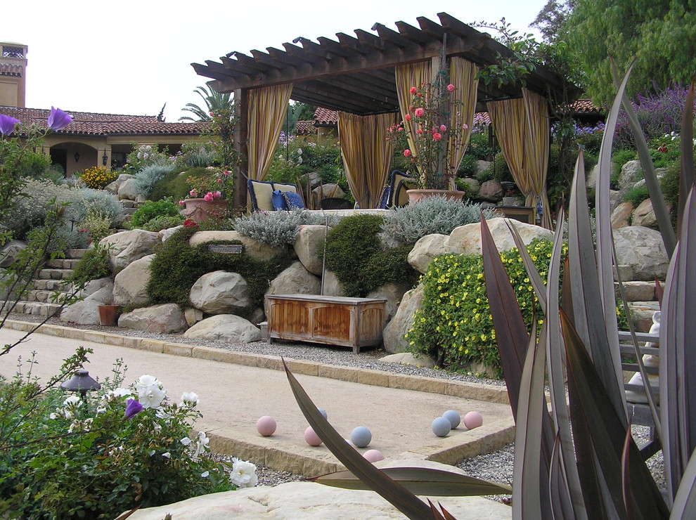 Immagine di un grande giardino mediterraneo dietro casa con un muro di contenimento, gazebo e ghiaia