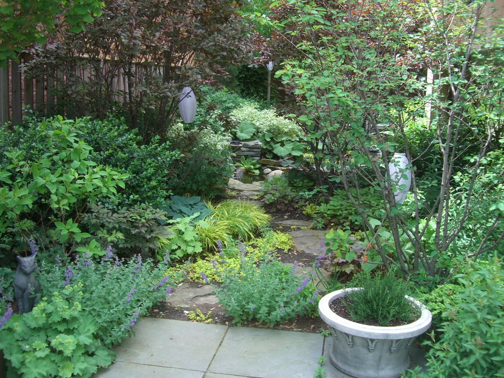 Réalisation d'un grand jardin en pots latéral tradition l'été avec une exposition ensoleillée et des pavés en pierre naturelle.