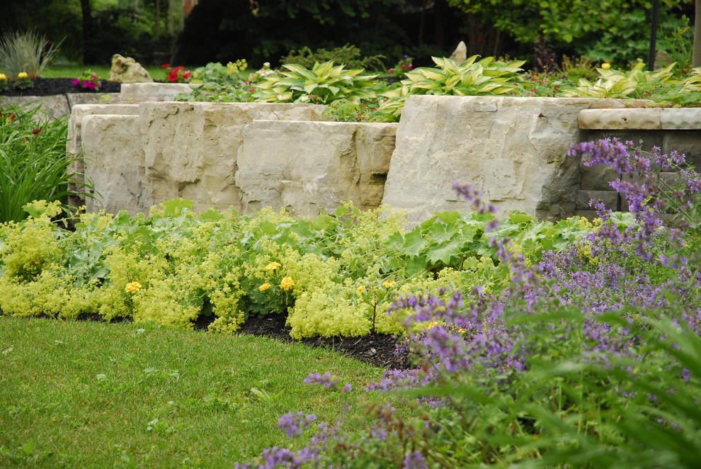 Inspiration för mellanstora klassiska trädgårdar i full sol framför huset på sommaren, med en stödmur och marksten i betong