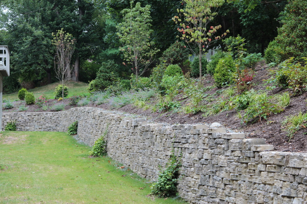 Foto di un grande giardino classico esposto in pieno sole dietro casa in estate con un muro di contenimento e pavimentazioni in cemento
