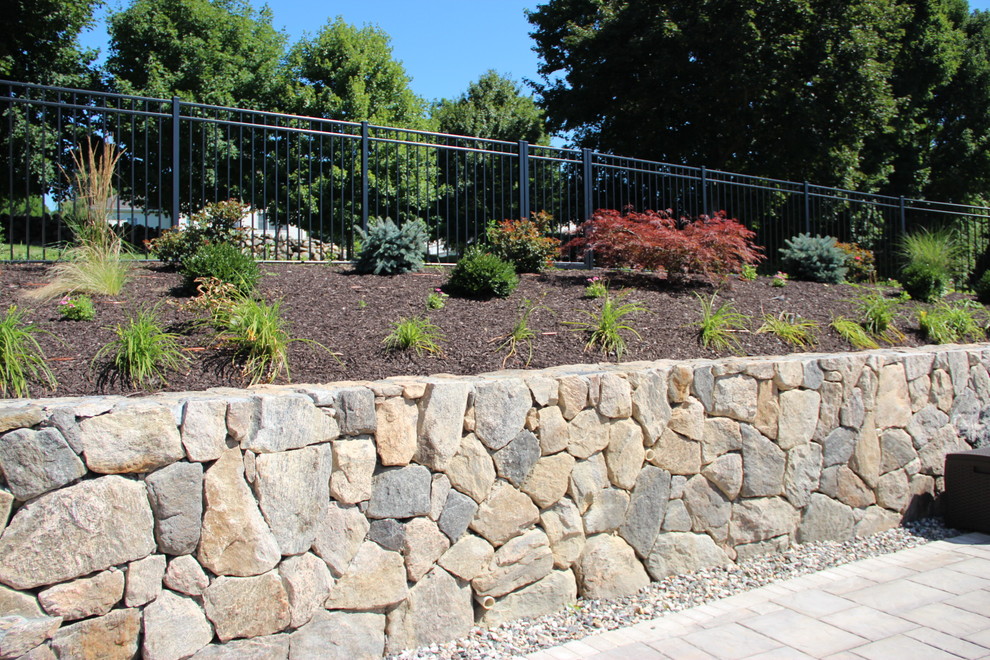 This is an example of a large traditional back xeriscape full sun garden for spring in New York with a retaining wall and concrete paving.