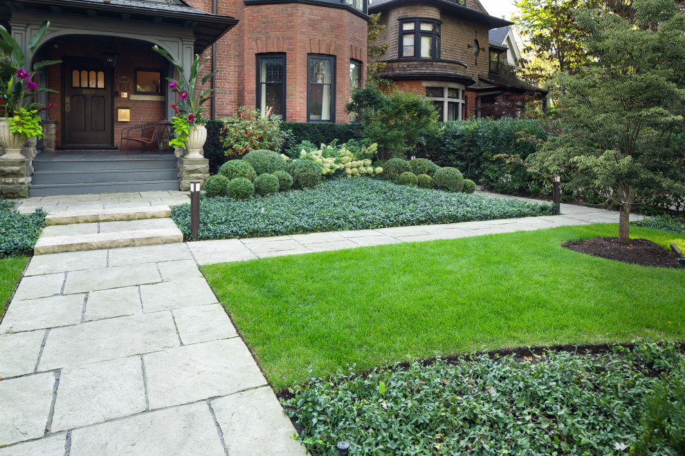 Large classic front partial sun garden for summer in Toronto with a pathway and natural stone paving.