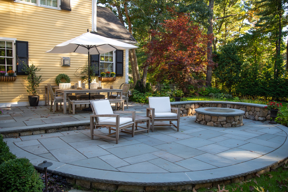 This is an example of a medium sized classic back patio in Boston with a fire feature and natural stone paving.