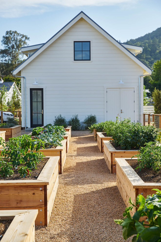 Diseño de jardín de estilo de casa de campo grande en verano en patio trasero con exposición total al sol, gravilla y huerto