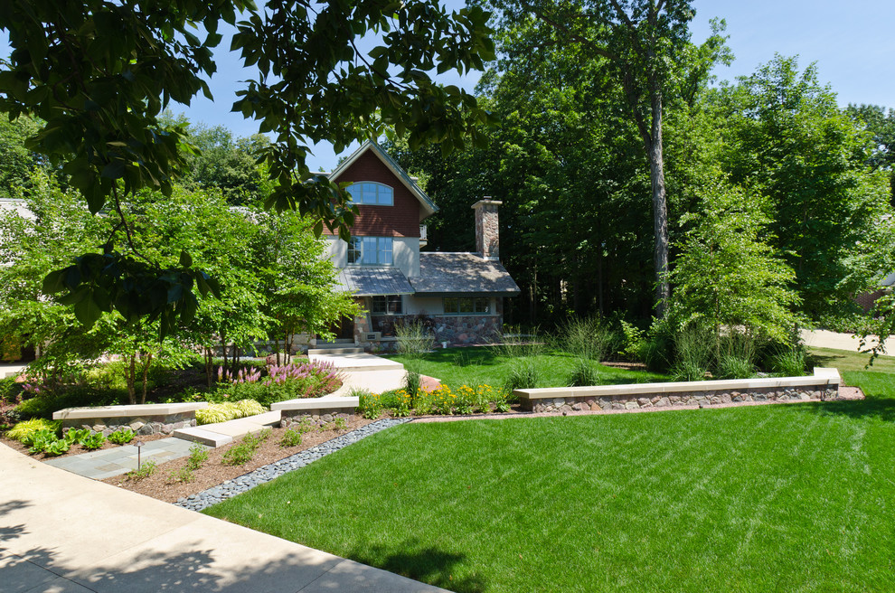Exempel på en stor amerikansk trädgård framför huset, med en stödmur och marksten i betong