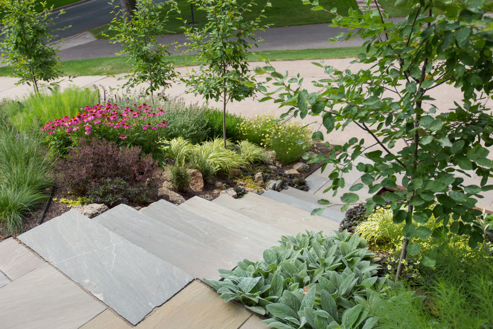 Immagine di un giardino minimal esposto in pieno sole davanti casa con un muro di contenimento e pavimentazioni in pietra naturale