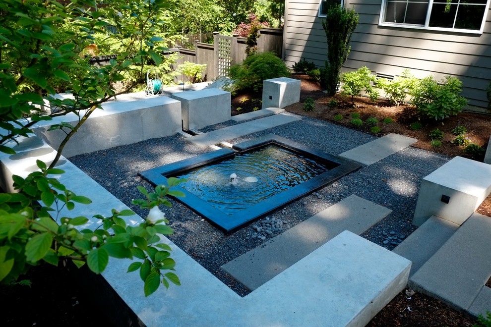 Ejemplo de jardín minimalista de tamaño medio en patio trasero con adoquines de hormigón, jardín francés, fuente y exposición parcial al sol