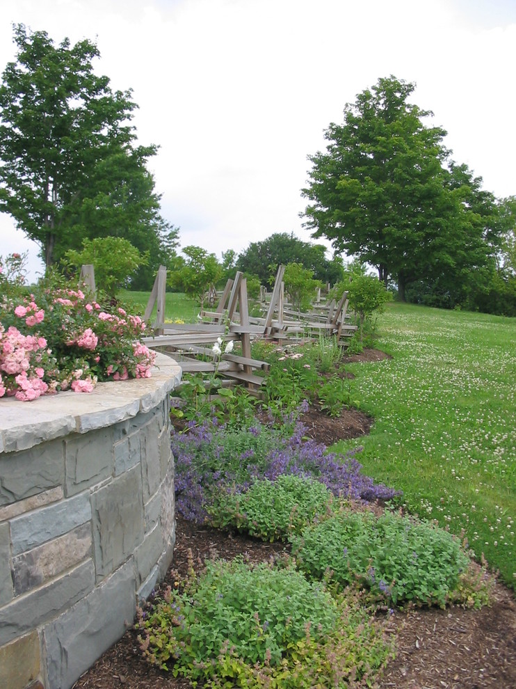 Foto di un ampio giardino country esposto in pieno sole dietro casa in primavera con un muro di contenimento e pacciame