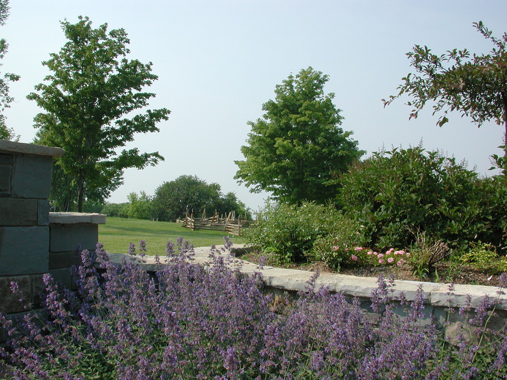 Immagine di un ampio giardino country esposto in pieno sole dietro casa in primavera con un muro di contenimento e pavimentazioni in pietra naturale