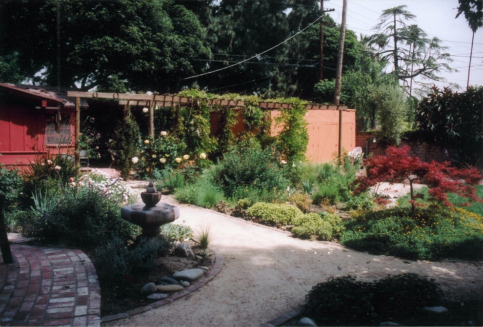 Bild på en stor medelhavsstil trädgård i delvis sol som tål torka och framför huset på sommaren, med naturstensplattor och en fontän