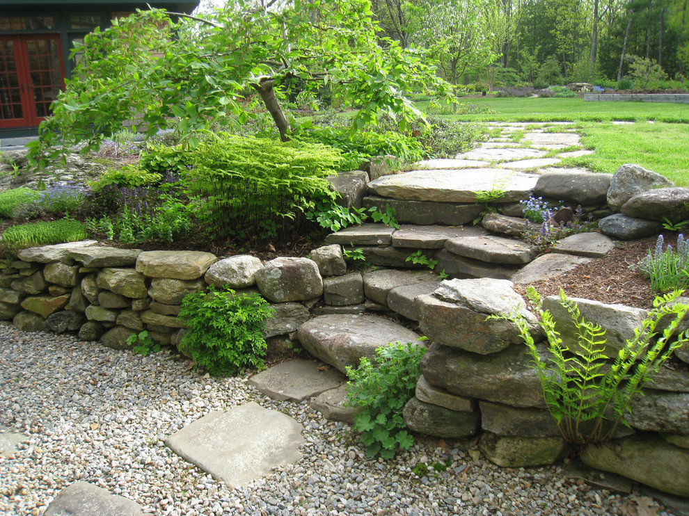 Modelo de jardín clásico de tamaño medio en verano en patio delantero con adoquines de piedra natural, exposición parcial al sol y muro de contención