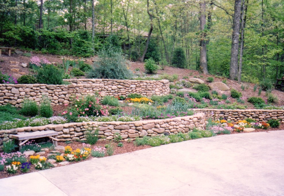 Modelo de jardín rústico de tamaño medio en verano en patio trasero con jardín francés, adoquines de piedra natural y muro de contención