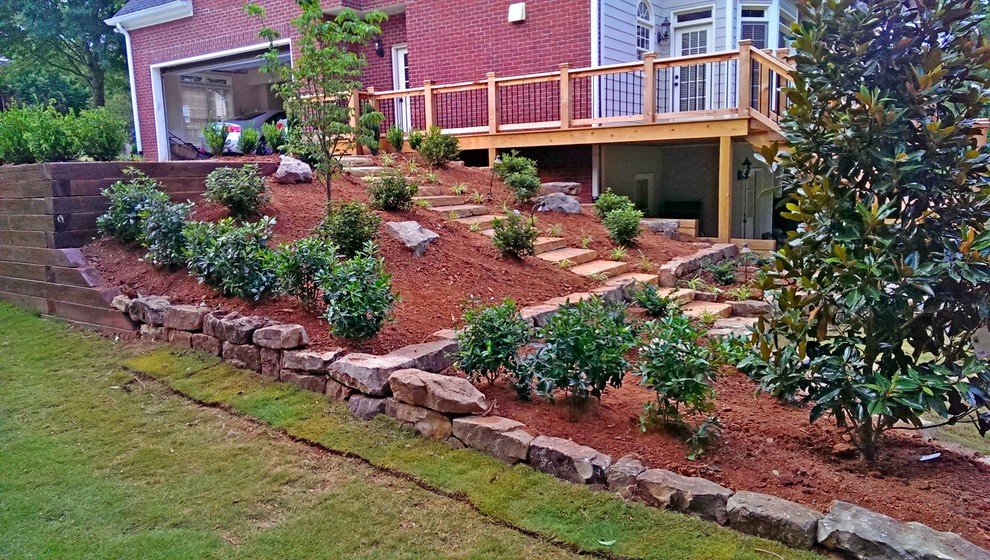 Стильный дизайн: большой солнечный регулярный сад на заднем дворе в классическом стиле с подпорной стенкой, хорошей освещенностью и покрытием из каменной брусчатки - последний тренд