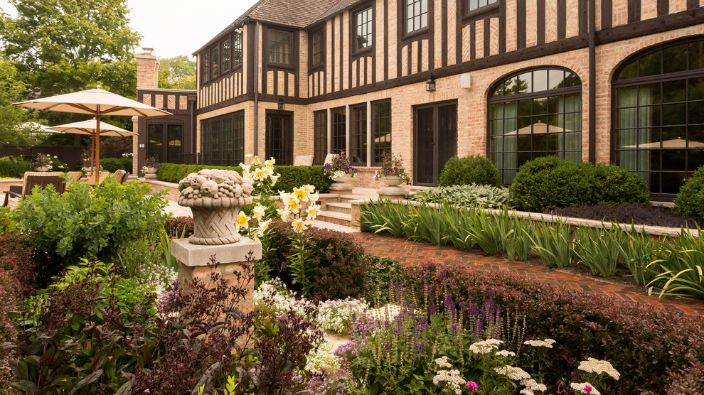 Aménagement d'un grand jardin arrière classique l'été avec un mur de soutènement, une exposition ensoleillée et des pavés en brique.