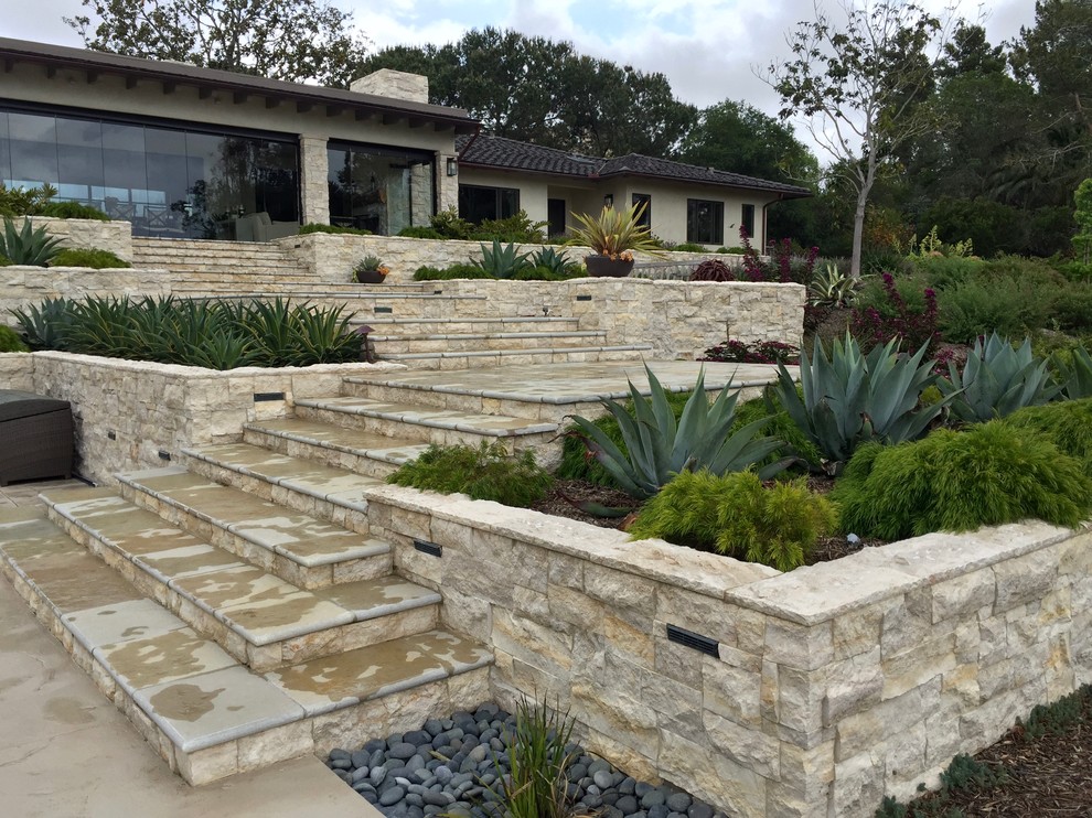 This is an example of an expansive contemporary back xeriscape full sun garden in San Diego with a retaining wall and natural stone paving.