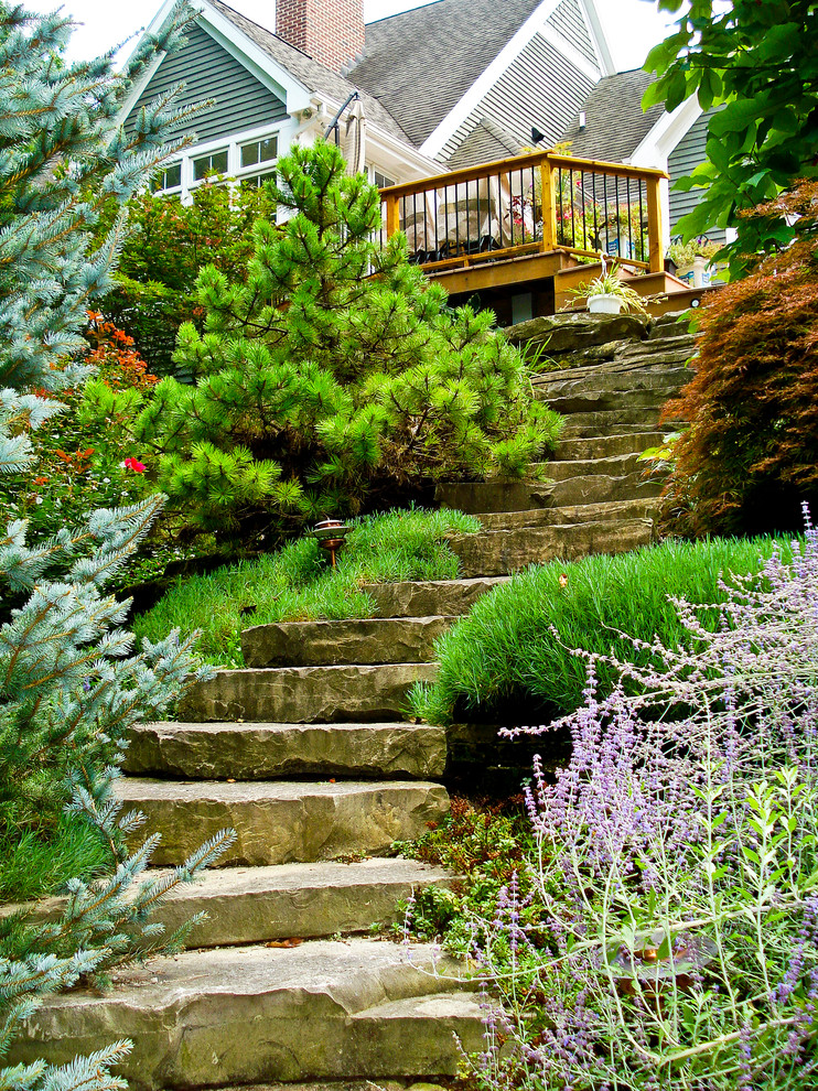 Large classic sloped full sun garden for summer in Grand Rapids with a retaining wall and natural stone paving.