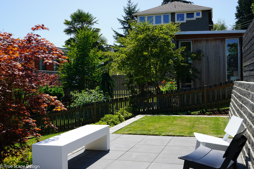 Medium sized modern sloped full sun garden for summer in Seattle with a retaining wall and concrete paving.