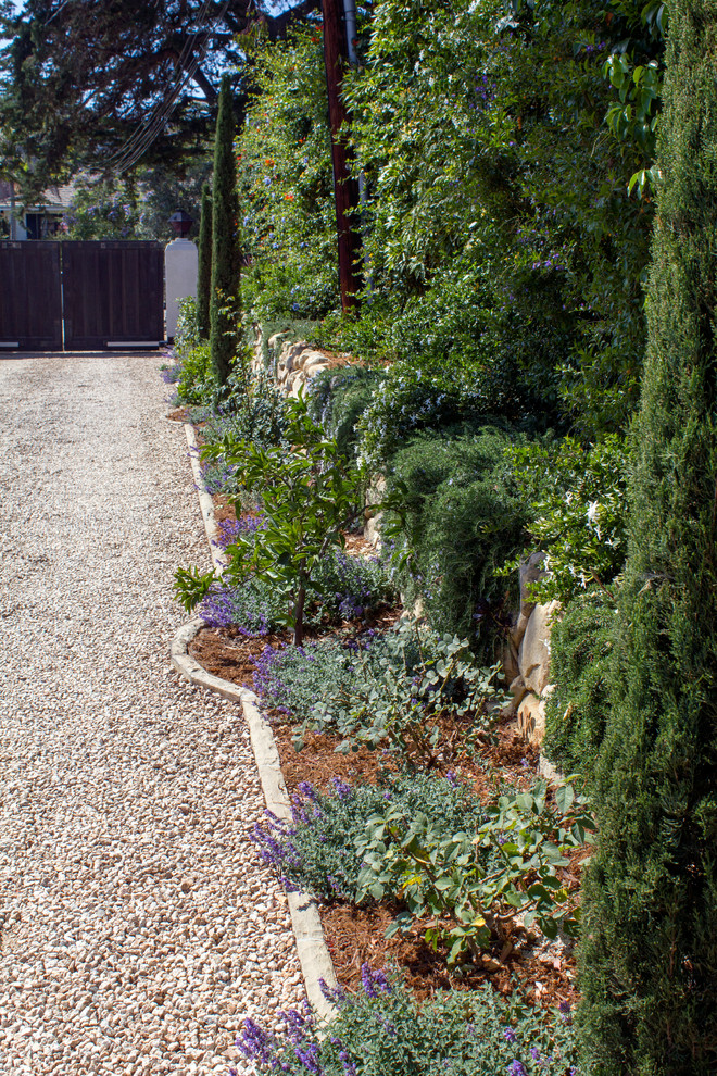 Diseño de jardín mediterráneo de tamaño medio en verano en patio delantero con jardín francés, muro de contención, exposición parcial al sol y gravilla